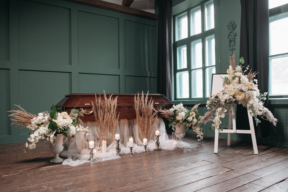 A floral arrangement inside a room featuring two large white vases filled with white roses, lilies, and greenery, complemented by pampas grass and other dried elements. The flowers are fresh, with del